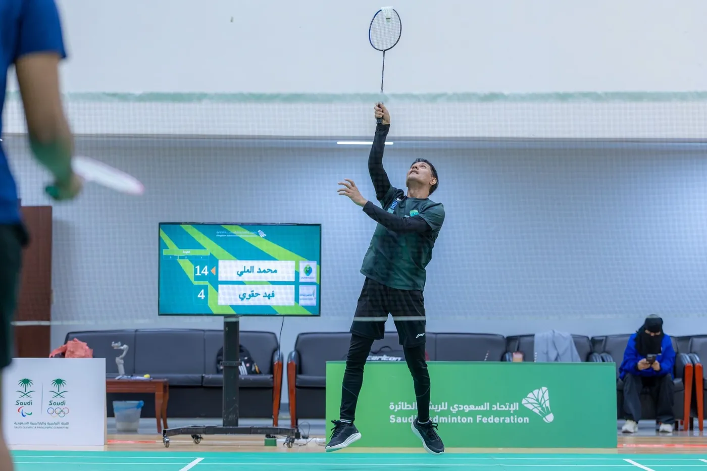 Spieler beim Aufschlag neben einer Live-Anzeigetafel bei einer Veranstaltung der Saudi Badminton Federation